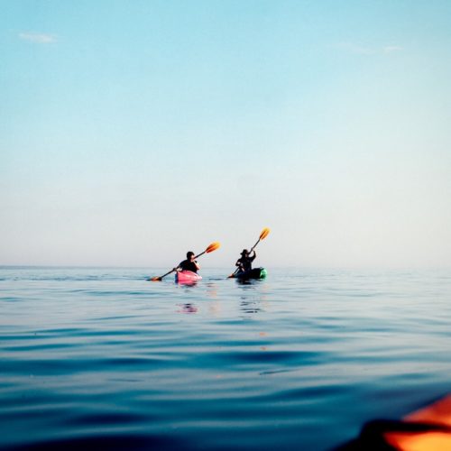 person in black wet suit riding on kayak on blue sea during daytime